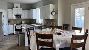 Uma cozinha com armários brancos, uma mesa de jantar com toalha de mesa florida e um relógio na parede.