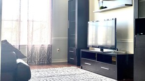 Uma sala de estar com uma televisão de tela plana grande, armários de madeira escura e um tapete estampado.