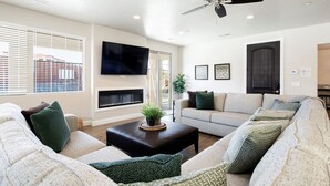 A living room with a fireplace, a flat-screen TV, and a ceiling fan. - Paradise Village 51, Private 20x40 Pool & Sport Court (Santa Clara)
