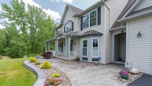 A two-story house with a covered porch, stone walkway, and a landscaped garden with various plants and flowers. - Private Family Retreat, Pool, Pickleball, 10 acres, 15 Min. from Rochester (Macedon)