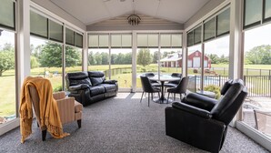 A covered patio with a ceiling fan, a black leather sofa, a striped armchair, and a dining table with chairs. - Private Family Retreat, Pool, Pickleball, 10 acres, 15 Min. from Rochester (Macedon)