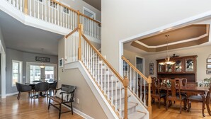 A spacious living area with a wooden staircase, a dining table with chairs, and a kitchen area with wooden cabinets. - Private Family Retreat, Pool, Pickleball, 10 acres, 15 Min. from Rochester (Macedon)