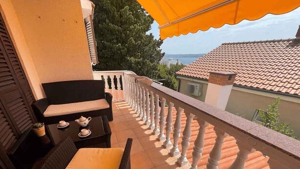 Un balcón con barandilla blanca, una mesa con tetera y una silla.