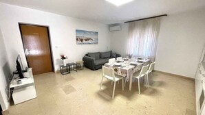 A modern living room with a dining area, a grey sofa, a painting on the wall, and a door. - Holiday apartment with air conditioning and sea views (Dramalj)