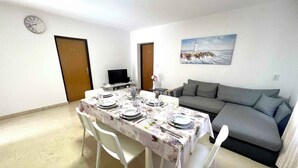 A dining area with a table set for four, a grey sofa, a painting of a lighthouse, and a clock on the wall. - Holiday apartment with air conditioning and sea views (Dramalj)