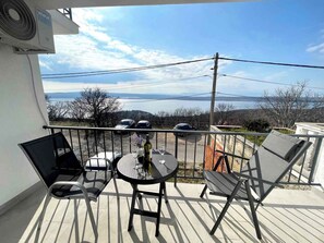 Een balkon met een tafel en stoelen, met uitzicht op een schilderachtig waterlandschap en heuvels.