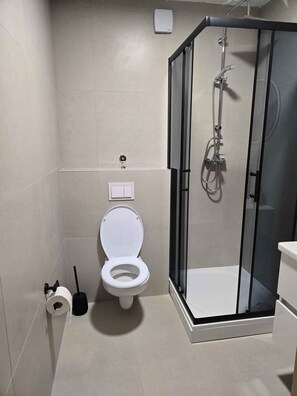 Moderni kylpyhuone, jossa on wc, suihkukaappi ja wc-paperiteline.