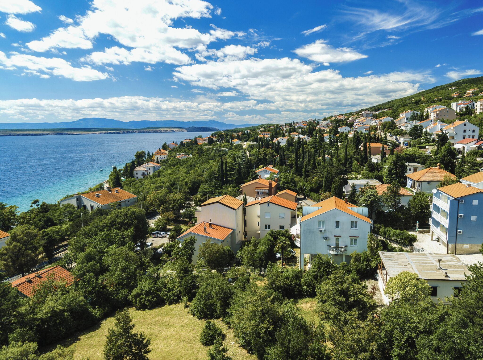 Ett bostadsområde vid kusten med hus, träd och utsikt över havet.