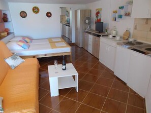 Una habitación compacta con cama, una mesita con botella y vaso, kitchenette y sofá.