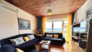 A living room with a wooden ceiling, a sofa set, a coffee table, a view of the sea through a large window, and a cabinet with glass doors. - Holiday apartment Spacious with terrace and views (Dramalj)