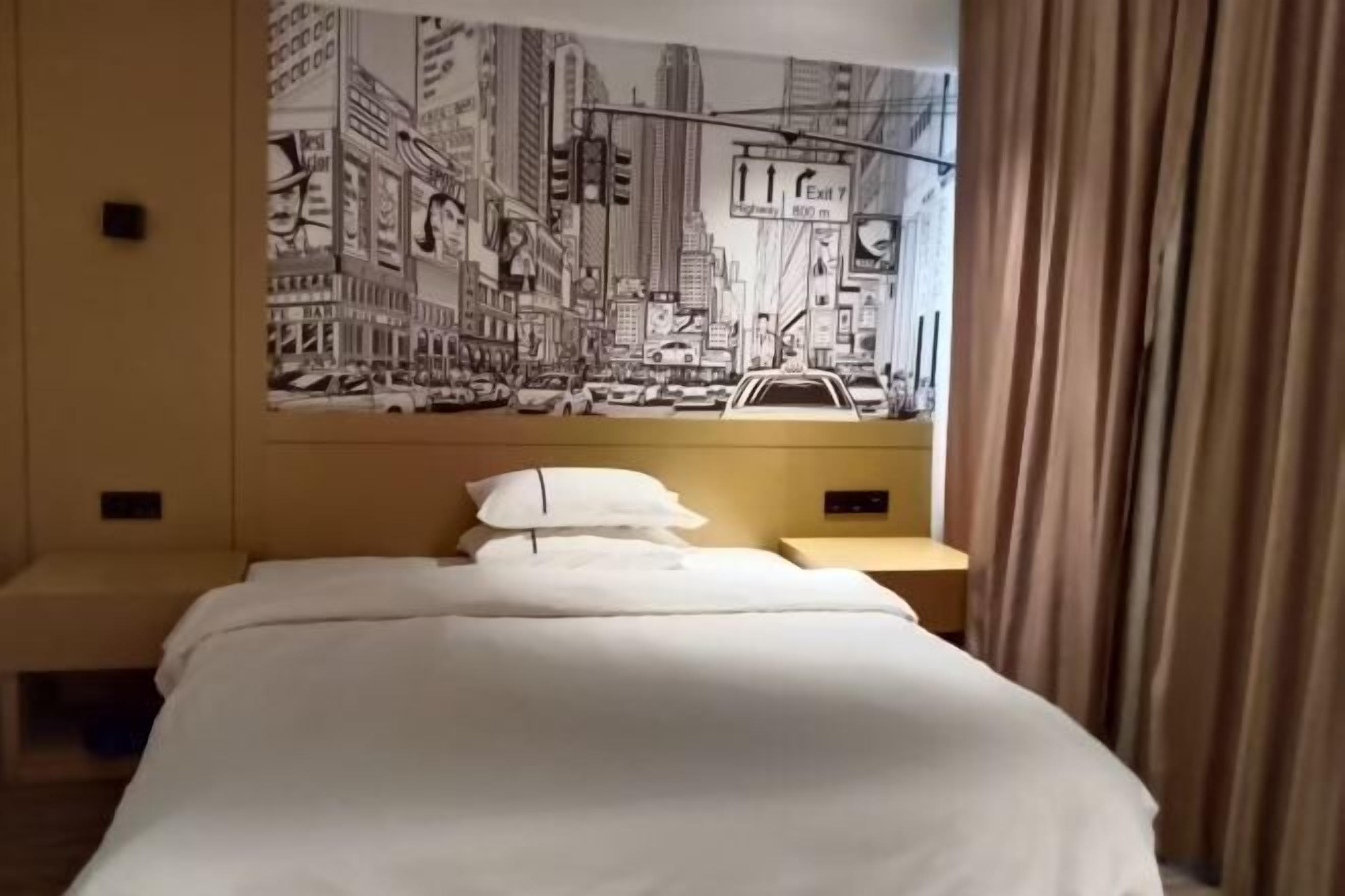 Une chambre d’hôtel avec un lit, une table de chevet, un téléphone fixé au mur et une grande fresque représentant un paysage urbain.