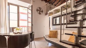 A modern living room with a sofa, a dining table with chairs, a staircase, and a clock on the wall.