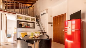 A modern kitchen with a red refrigerator, a dining table with chairs, and a staircase leading to an upper level.