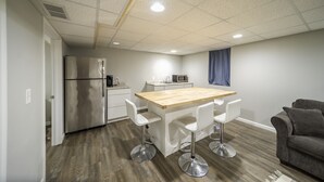 Una cocina moderna con una isla de madera, taburetes blancos tipo bar, un refrigerador y un microondas.
