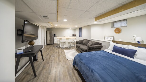 Una habitación moderna con cama, escritorio, televisión, kitchenette y un pequeño comedor.