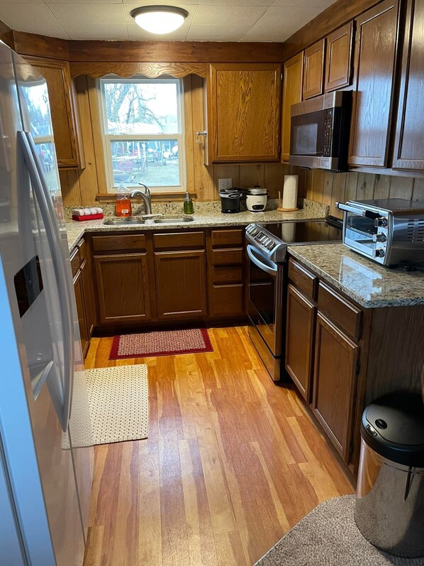 A kitchen with wooden cabinets, a stainless steel refrigerator, a microwave, a toaster, and a sink.
