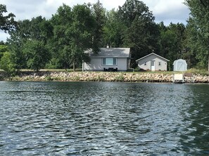 A lakeside cabin with a dock, surrounded by trees and a stone wall.
