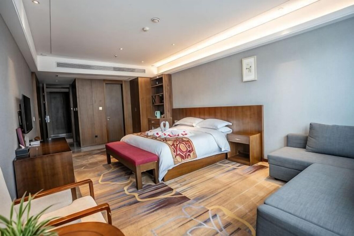 A modern hotel room with a large bed, a sofa, a desk, and a TV.