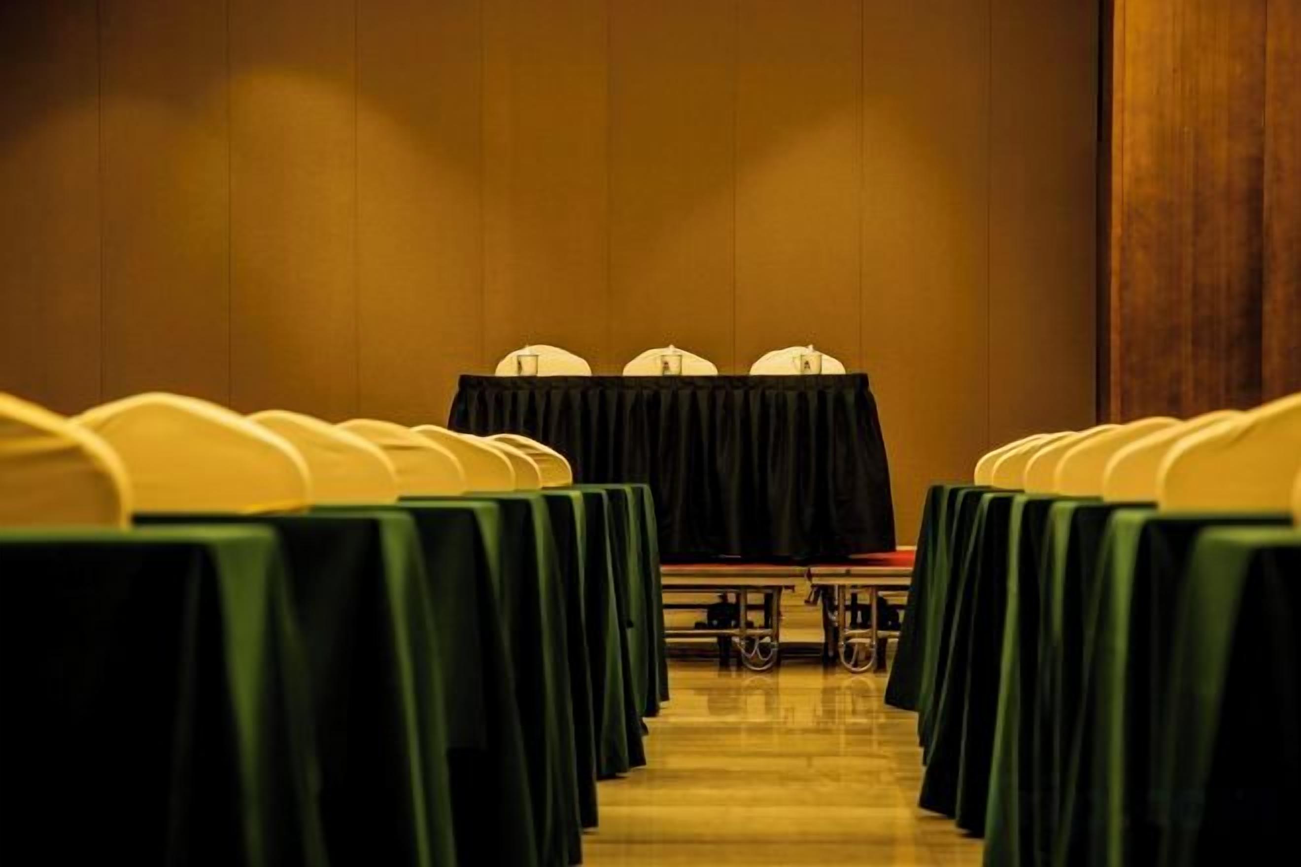 A conference room with rows of tables and chairs, a podium, and a carpeted floor.