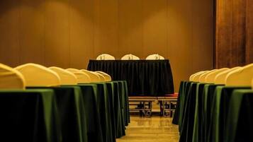 A conference room with rows of tables and chairs, a podium, and a carpeted floor.