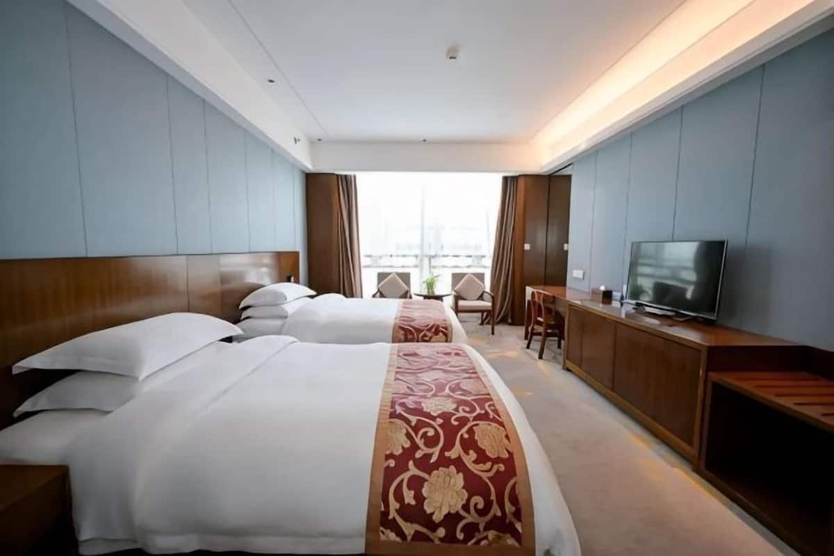 A hotel room with two beds, a TV, a desk, and a view of the city.