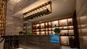 Zona de recepción de hotel con suelo de mármol, mostrador de recepción, área de asientos con sillas y una pared con estanterías que exhiben diversos objetos.