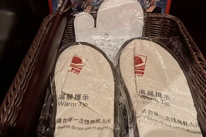 A wicker basket containing two pairs of slippers with a warning label.