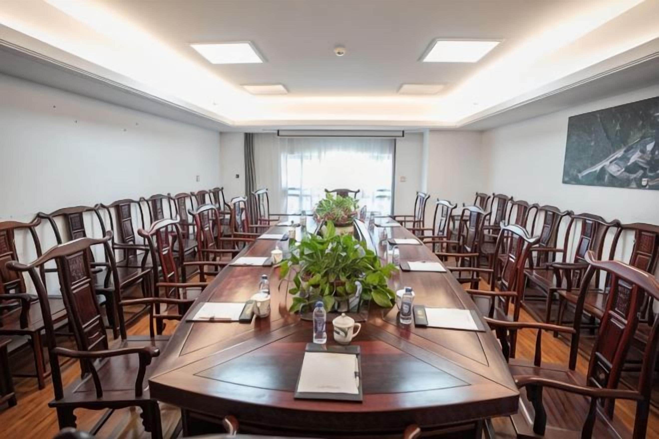 Un salón de conferencias con una larga mesa, sillas y un centro de mesa con planta.