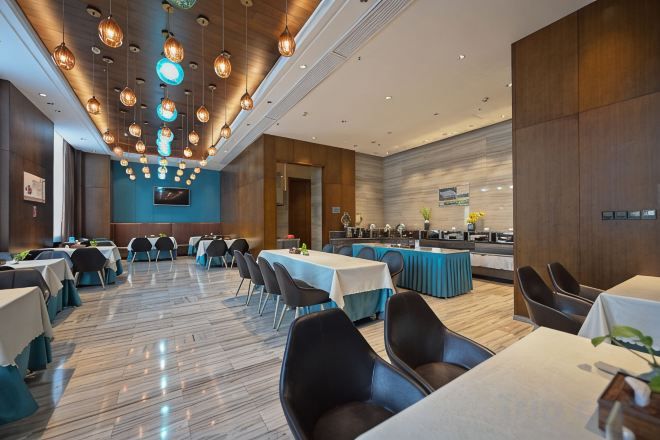 Ein moderner Hotel-Speisebereich mit mehreren Tischen, Stühlen und einer zentralen Bar.