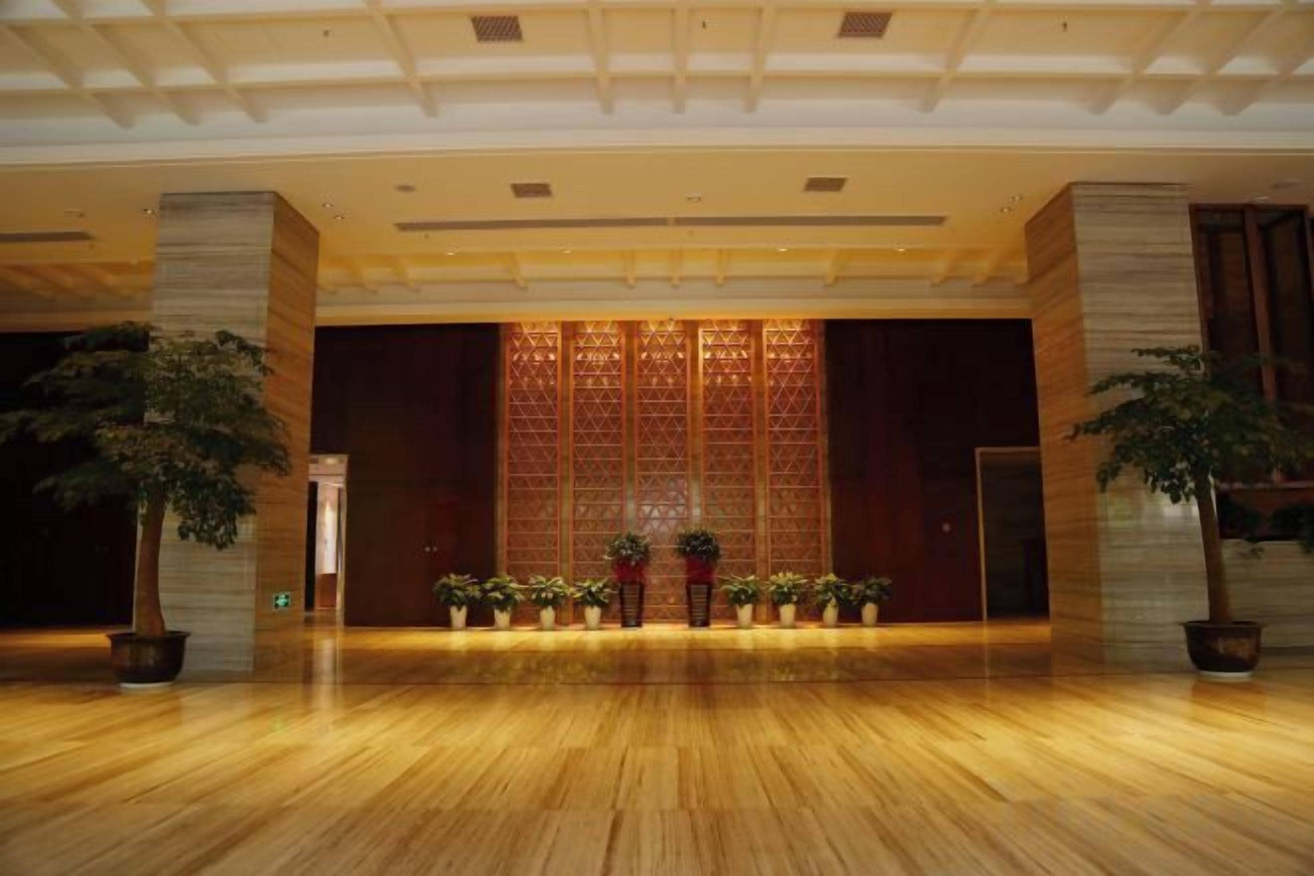 Un vestíbulo amplio con piso de madera pulida, un gran muro decorativo y plantas en macetas.
