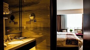 Una habitación de hotel moderna con un tocador de mármol, una cama grande con cabecera decorativa y vistas a la ciudad desde la ventana.