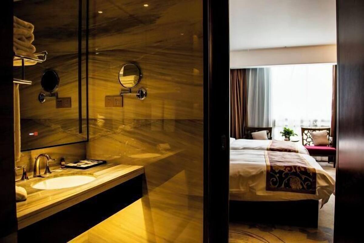 A modern hotel room with a marble vanity, a large bed with a decorative headboard, and a view of the city through the window.