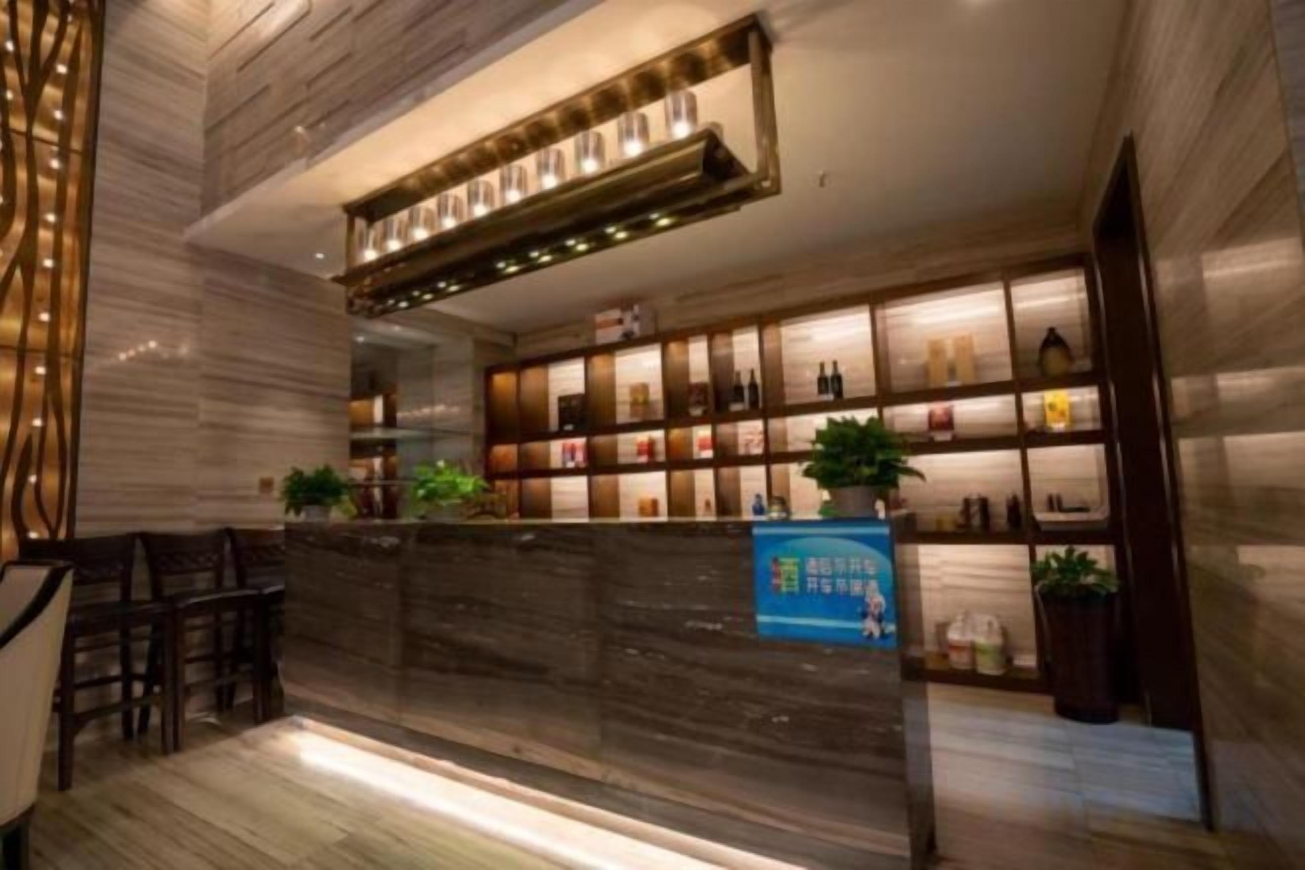 Een hotellobby met een receptiebalie, een zithoek en een wand met planken waarop diverse objecten staan.