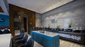 Un comedor de hotel moderno con una barra larga, varias sillas y una cocina al fondo.