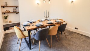 Comedor con mesa de madera dispuesta para seis personas, rodeada por seis sillas, una araña y apliques de pared.