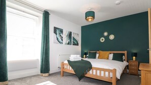 Un dormitorio con cama, mesita de noche, lámpara, radiador y una obra de arte en la pared.