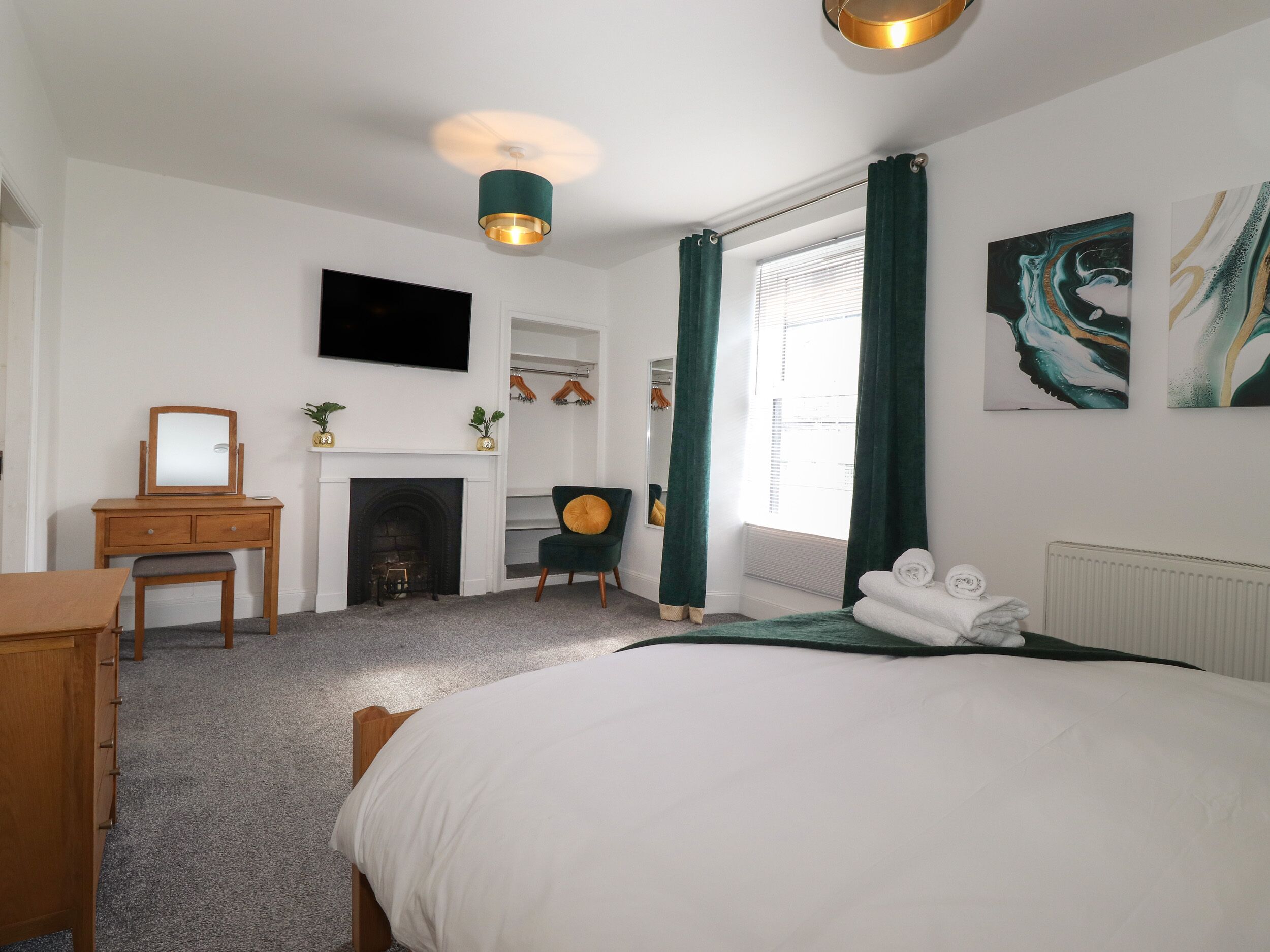 A bedroom with a bed, a dresser, a chair, a fireplace, and artwork on the walls.