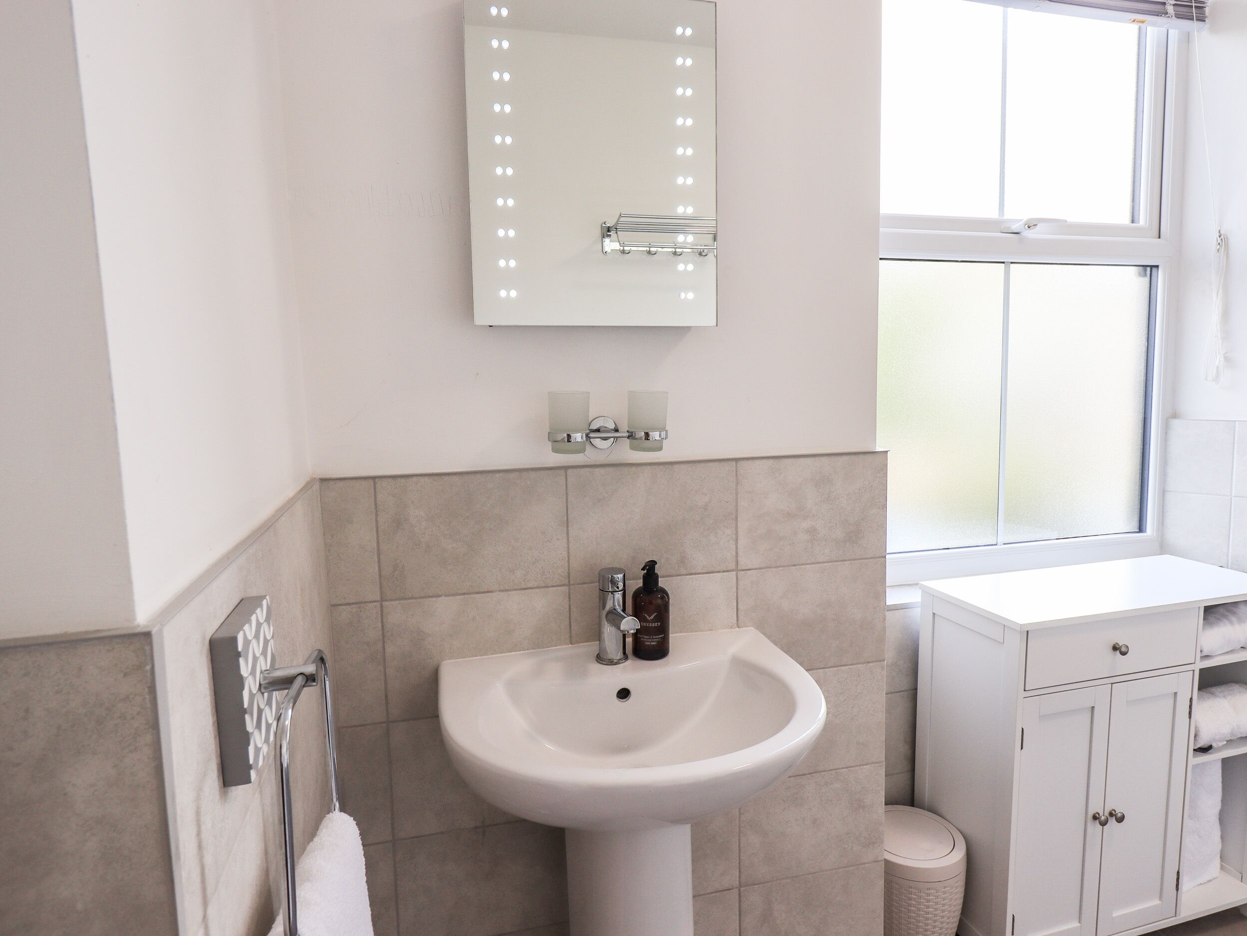 Ein Badezimmer mit Waschbecken, Spiegel mit Beleuchtung, Handtuchhalter und Fenster.
