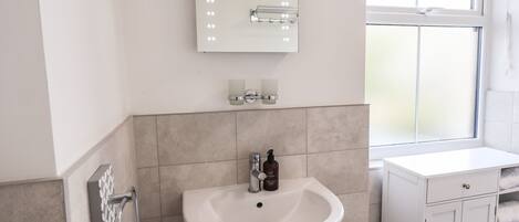 Ein Badezimmer mit Waschbecken, Spiegel mit Beleuchtung, Handtuchhalter und Fenster.