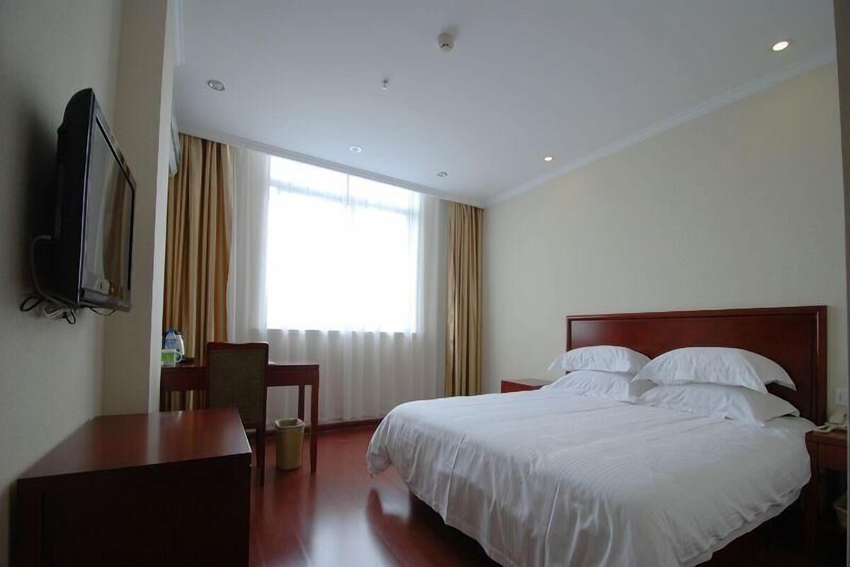 A hotel room with a bed, a desk, a chair, a television, and a window with curtains.