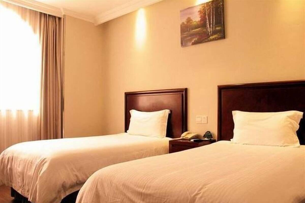 Ein Hotelzimmer mit zwei Betten, einem Bild an der Wand und einem Fenster mit Vorhängen.