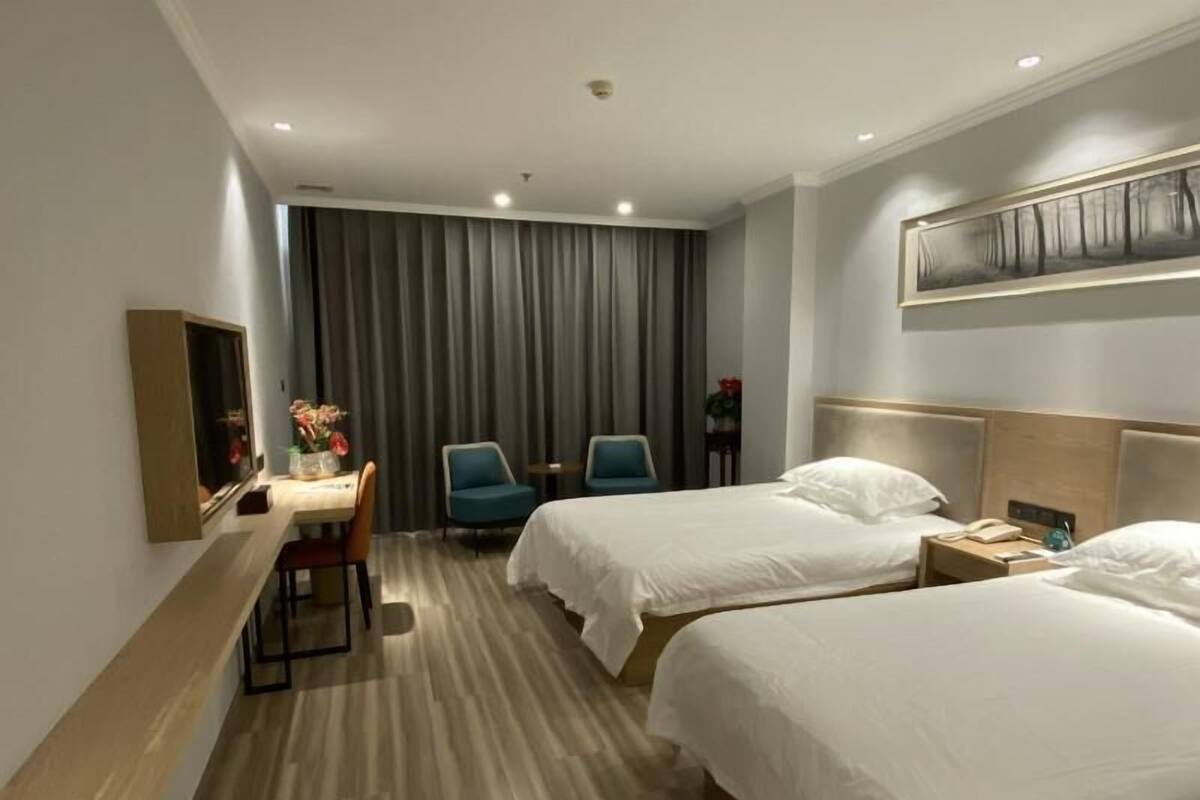 Ein Hotelzimmer mit zwei Betten, einem Schreibtisch, einem Stuhl, einem Bild an der Wand und einem Vorhang.