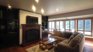 A living room with a fireplace, a sofa, a coffee table, and a bookshelf. - Welcome! Cozy large house to make memories of laughter and joy by the Big Blue! (South Haven)