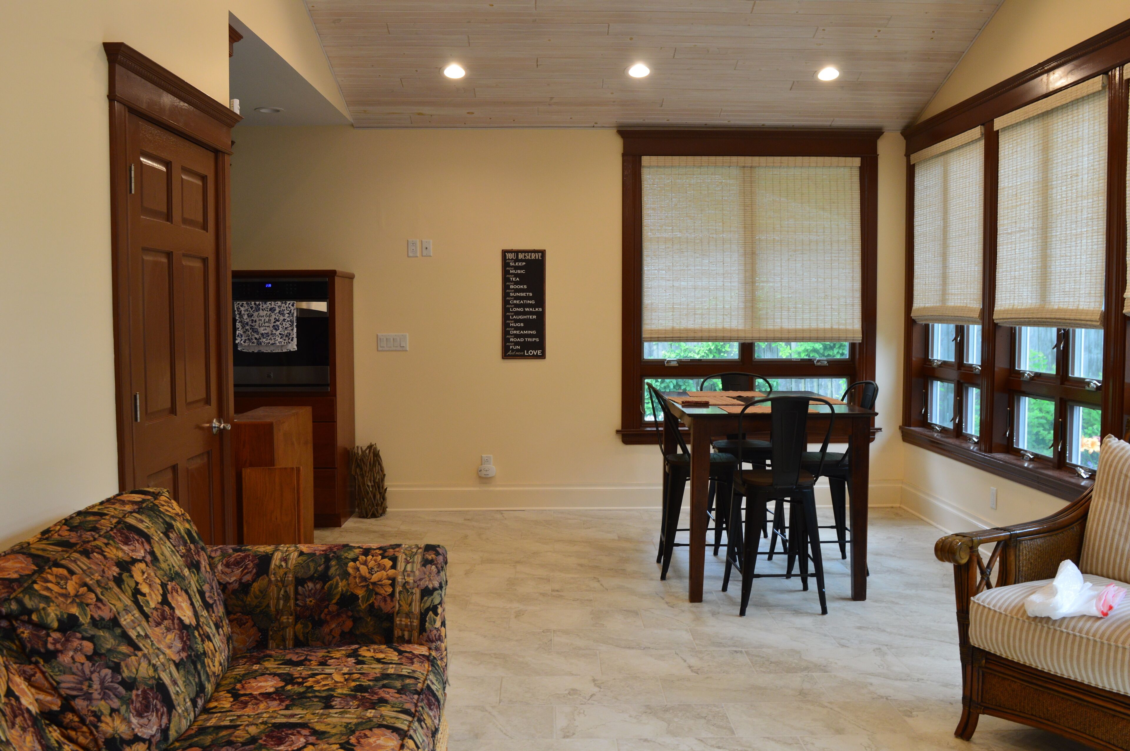 Un comedor con una mesa y sillas de madera, un sofá floral y una ventana con persianas.