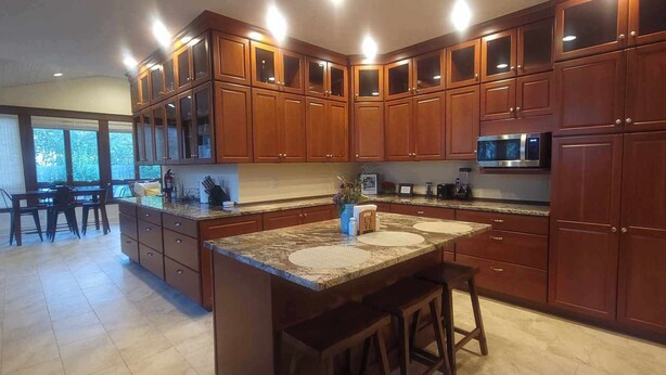 A kitchen with wooden cabinets, granite countertops, a microwave, and a dining area with chairs and a table. - Welcome! Cozy large house to make memories of laughter and joy by the Big Blue! (South Haven)