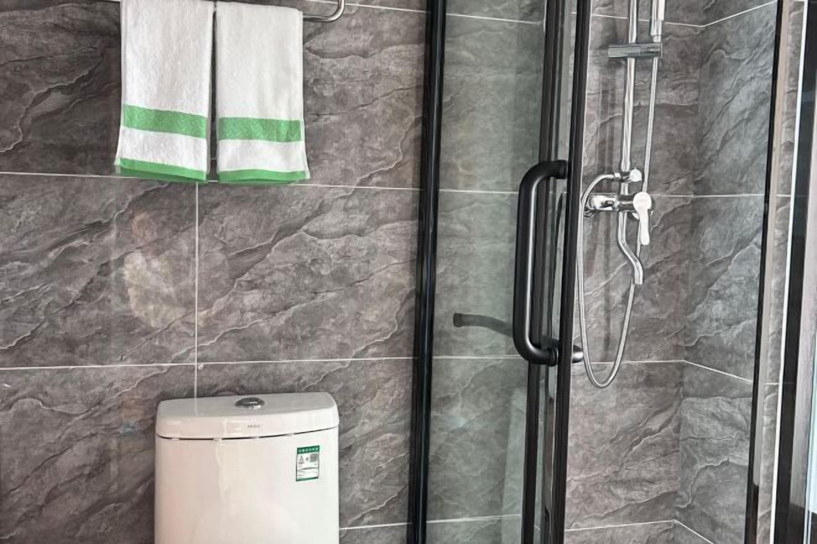 A bathroom with a glass shower enclosure, a towel rack with two towels, and a water heater.