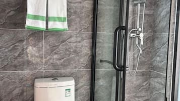A bathroom with a glass shower enclosure, a towel rack with two towels, and a water heater.