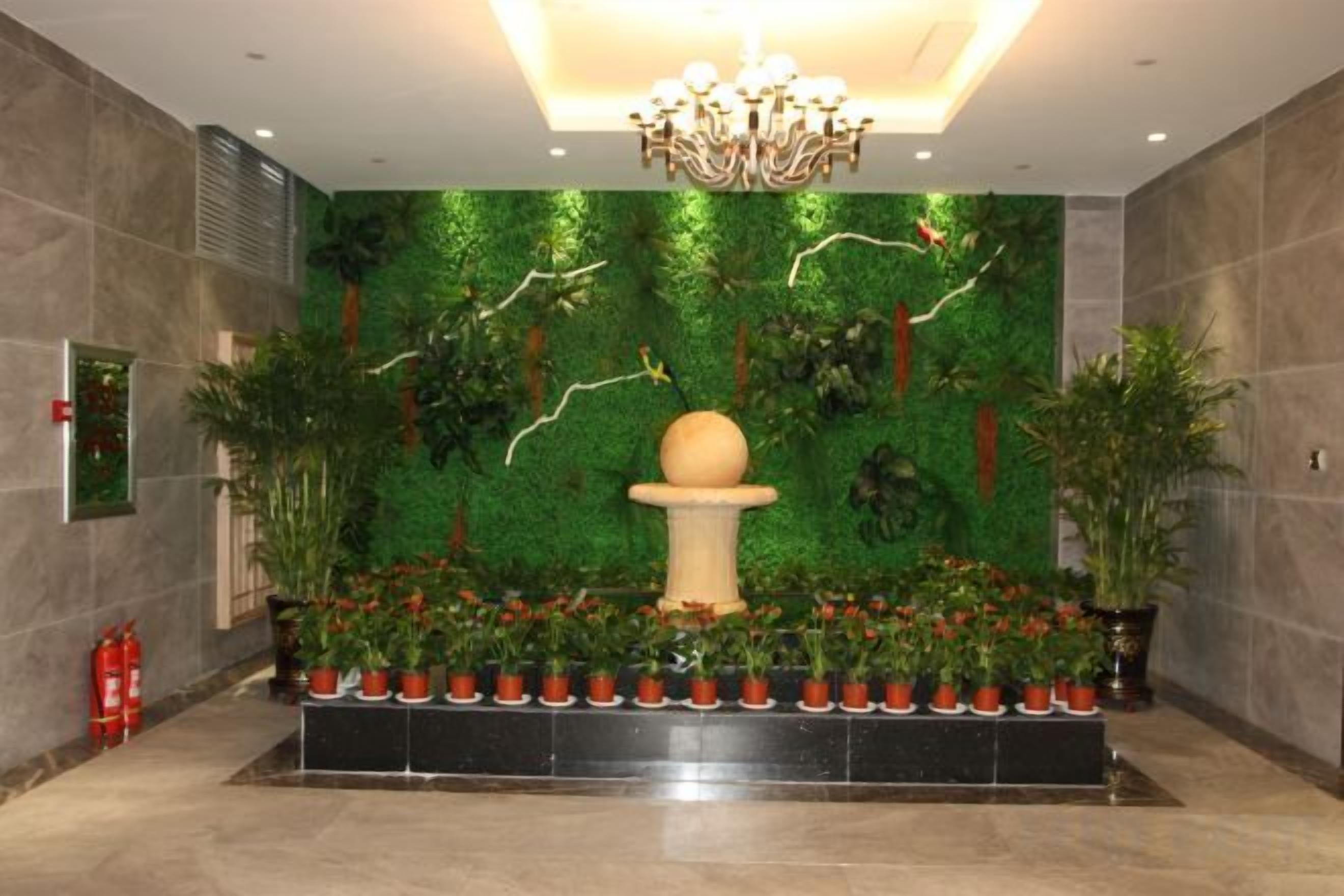 A lobby with a green wall, a central fountain, and potted plants.