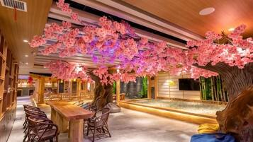 A restaurant with a long counter, chairs, and a decorative tree with pink flowers.