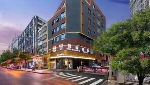 A modern hotel with a curved facade, multiple floors, and a prominent entrance with illuminated signage. - V8 Wisdom Hotel (Haikou CRV East Railway Station) (Haikou)
